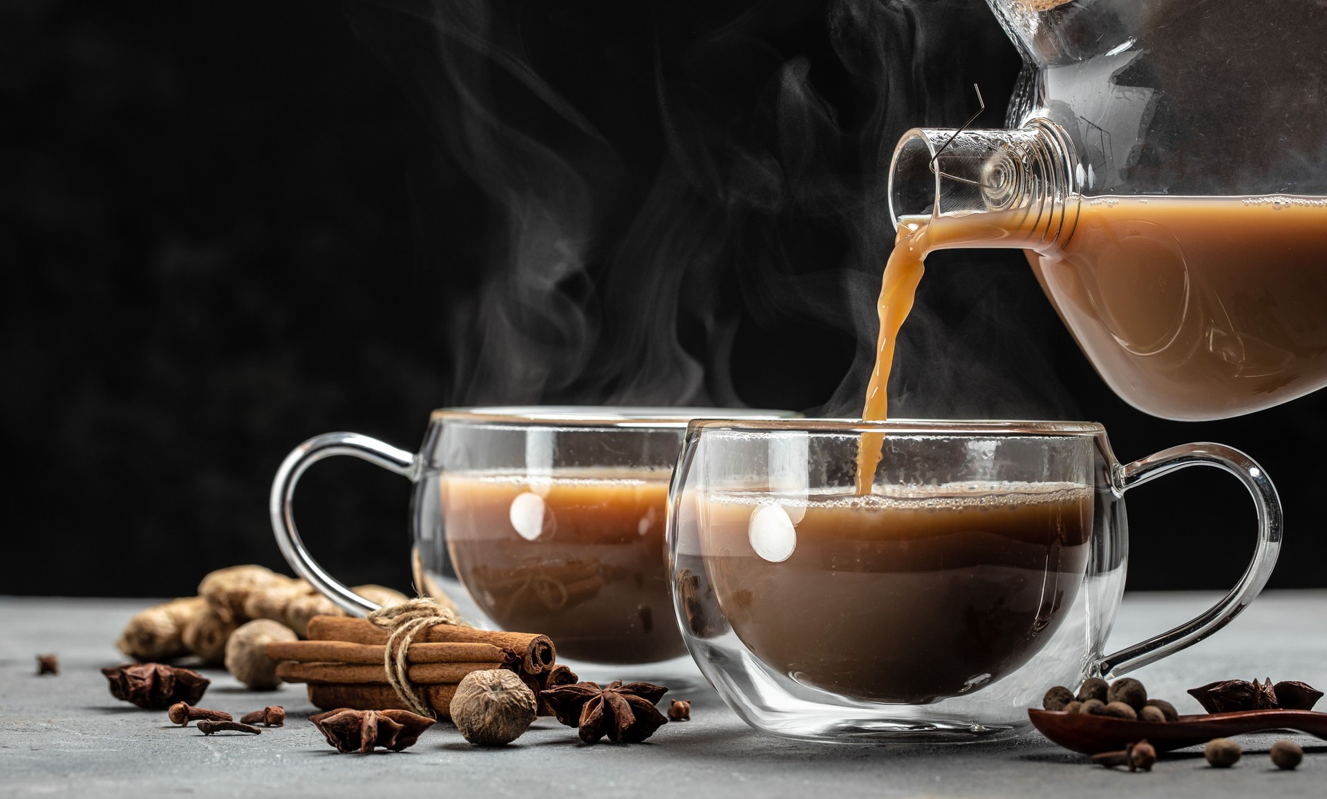 Indian masala chai tea. Hot masala chai spiced tea with milk and spices is poured into a glass glass on gray background. Long banner format. place for text